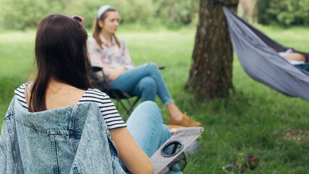 A group of friends relaxing outdoors on camping chairs and a hammock.