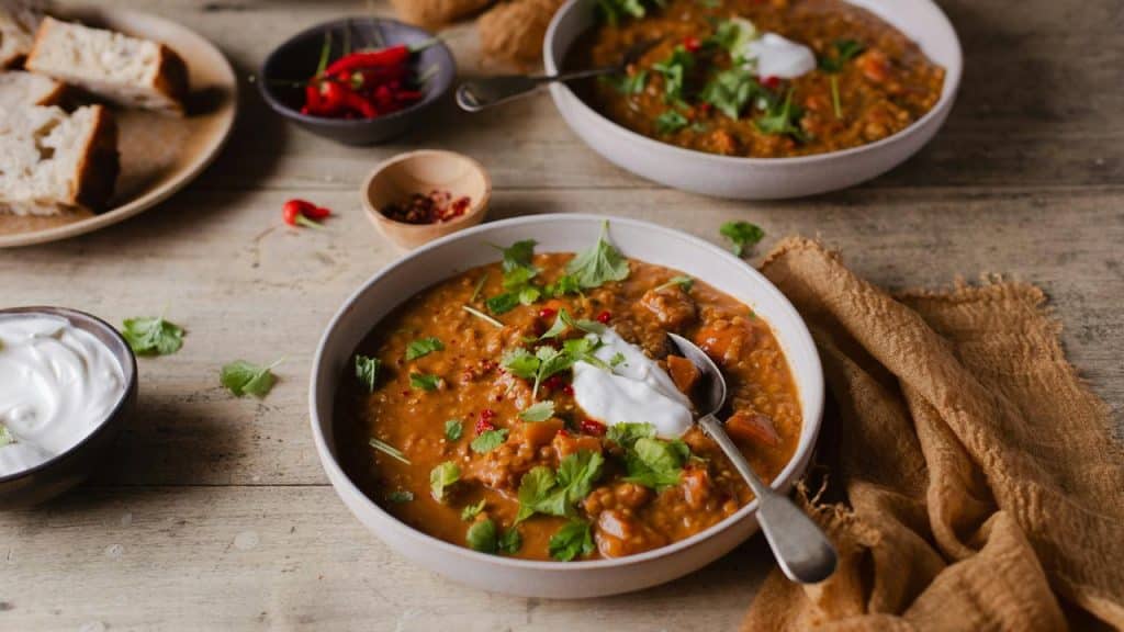 A bowl of lentil stew with bread and chili toppings.