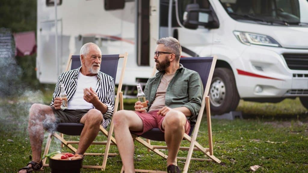 A photo of two men sitting outdoors with drinks by an RV.
