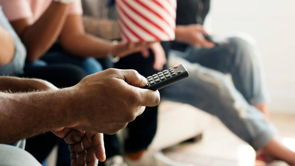 A person holding a TV remote with others nearby.