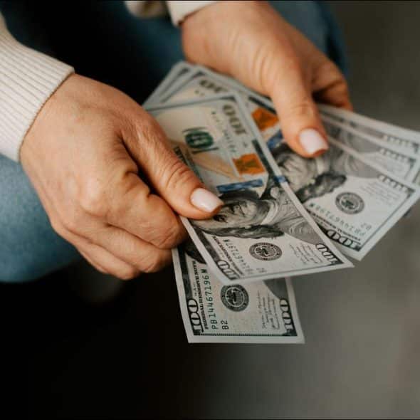 A person holding several $100 US dollar bills.