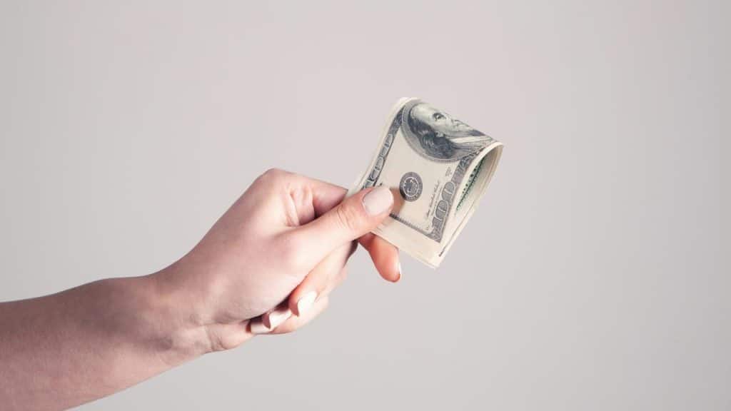 A person’s hand holding a stack of US dollar bills.