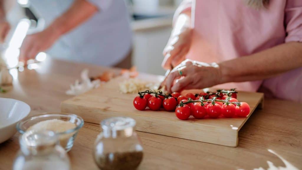 A person chopping cherry tomatoes on a wooden cutting board.