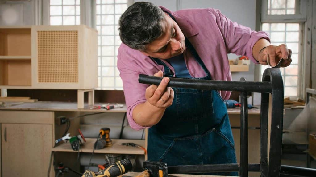 A man working on assembling or repairing a wooden chair in a workshop.