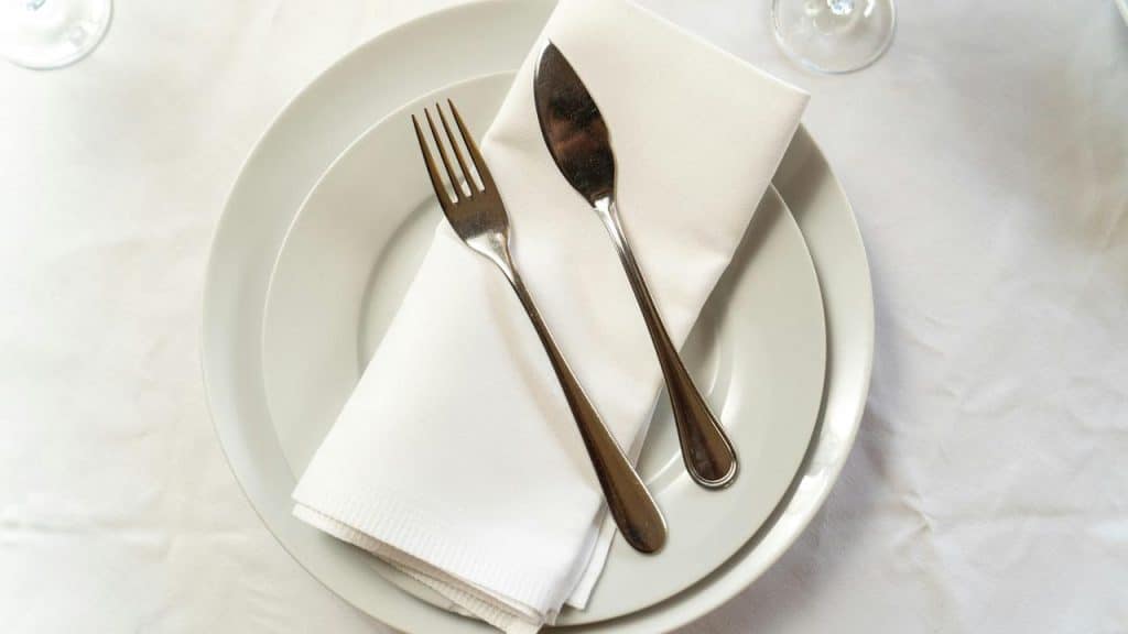 A fork and knife placed on a folded napkin over a white plate.