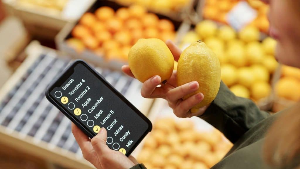 A person holding lemons while checking a digital shopping list on a phone.