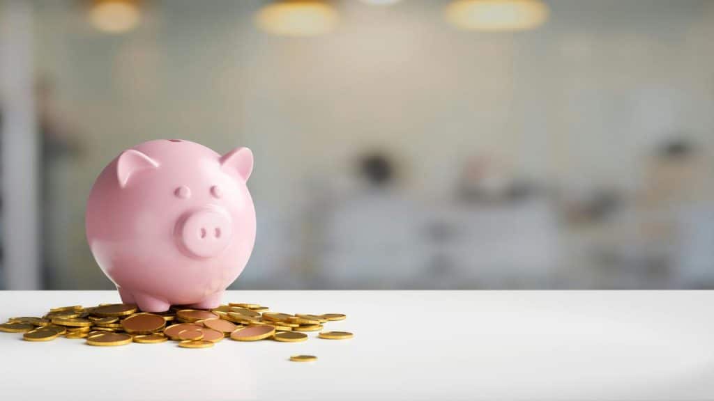 A pink piggy bank placed on a pile of gold coins.