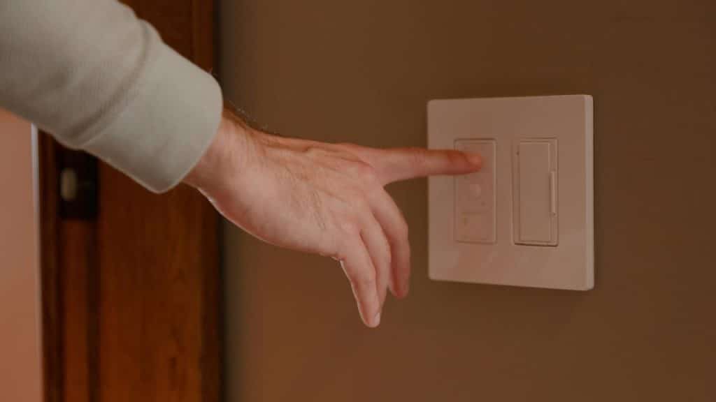 A person’s hand pressing a light switch on a wall.