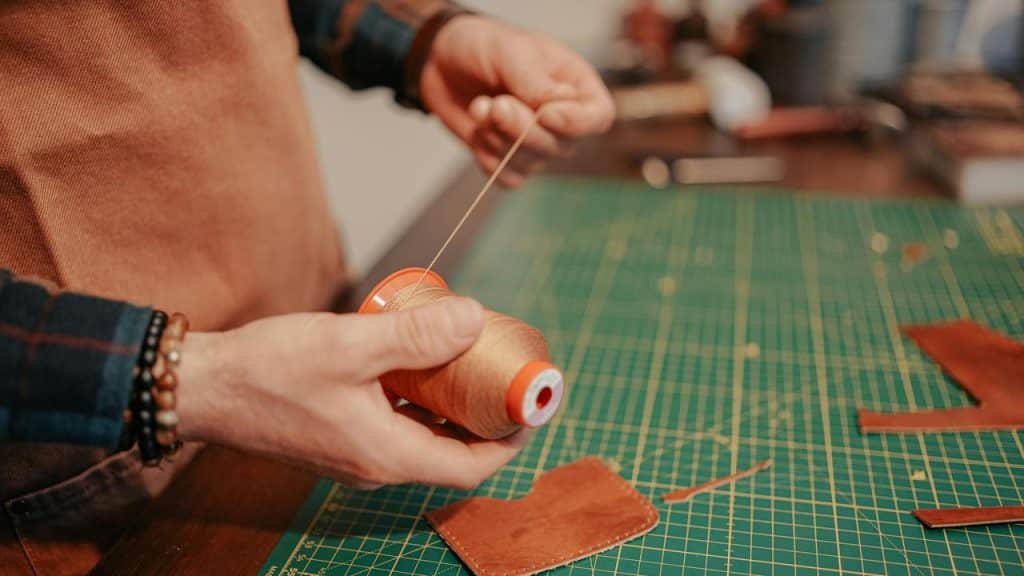 A person holding a spool of thread while working on a leather crafting project.
