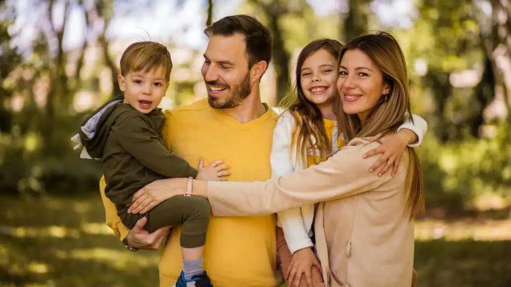 A happy family with two children posing outdoors and smiling.