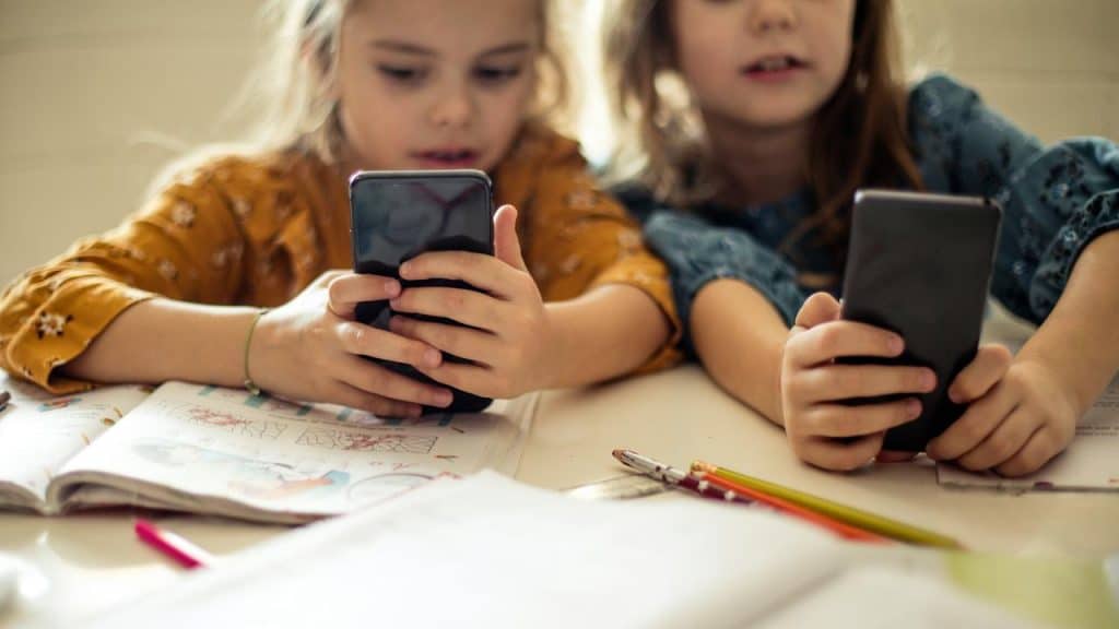 A pair of young girls using smartphones at a table with books.