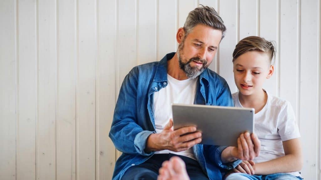 A father and son sitting together while looking at a tablet.