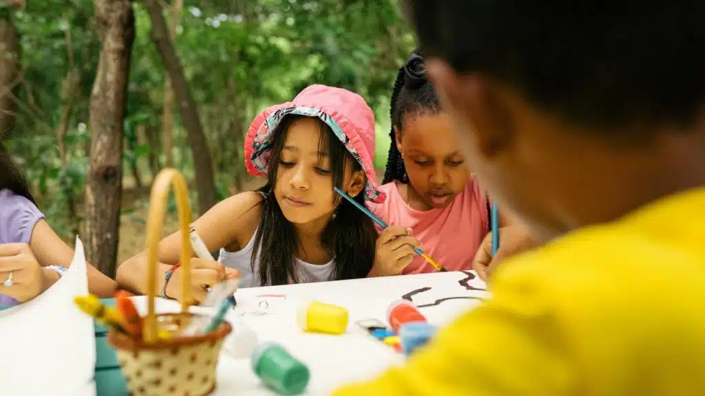 A group of children painting and drawing at a table outdoors.