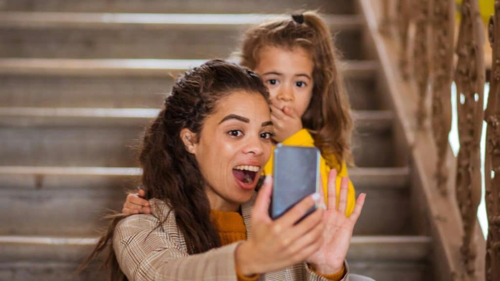A woman and a young girl looking surprised while taking a selfie on a phone.