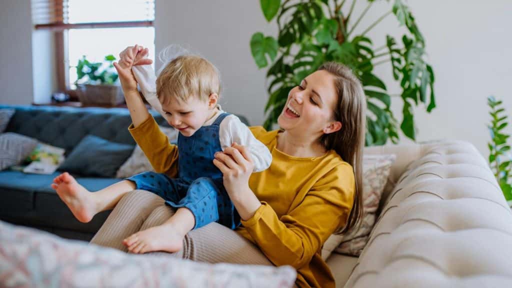 A smiling mother playing with her son on a couch.