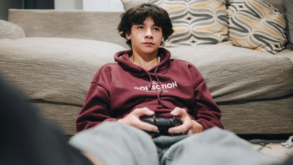 A teenage boy sitting on the floor playing video games with a controller.