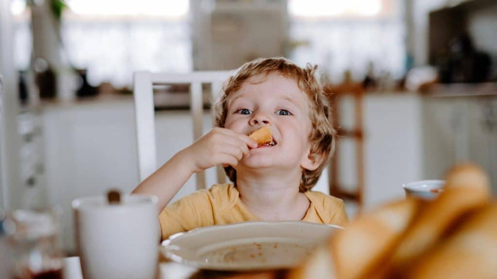 A young child eating bread at a dining table.
