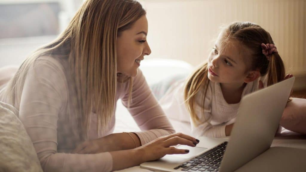 A mother and her daughter smiling while using a laptop together.
