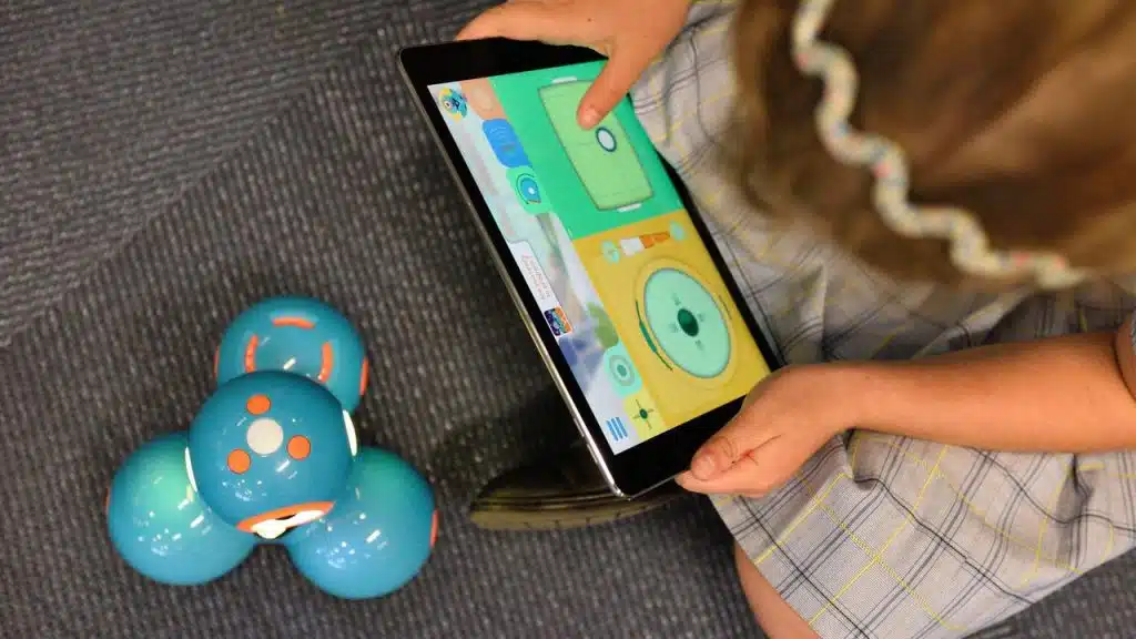 A child using a tablet to control a small blue robot.