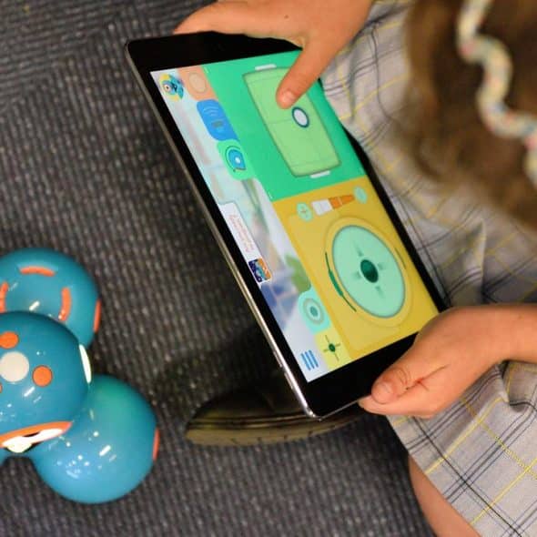 A child using a tablet to control a small blue robot.