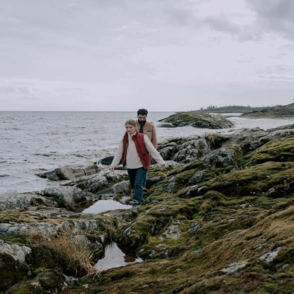 A man following a woman on a rocky shore.