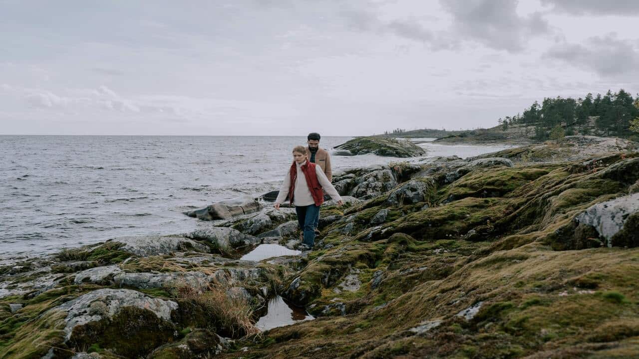 A man following a woman on a rocky shore.