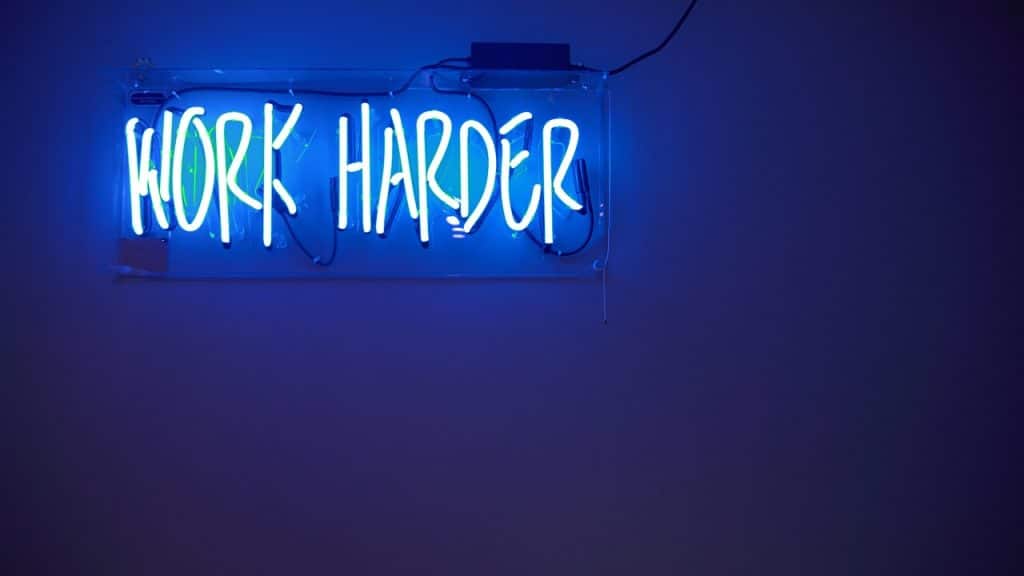 A neon light saying “work harder”