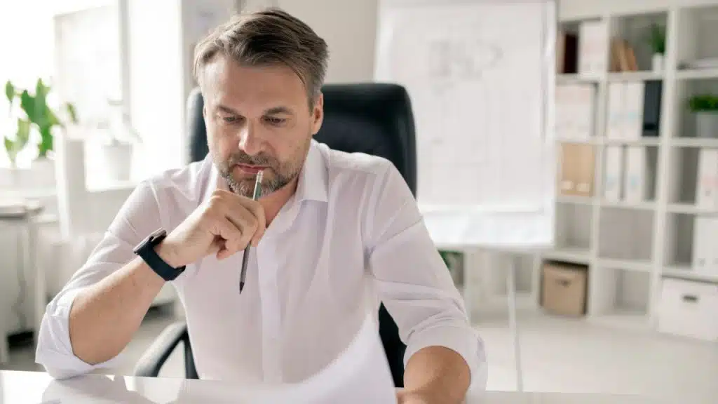 A thoughtful man with a beard is looking down at some papers.