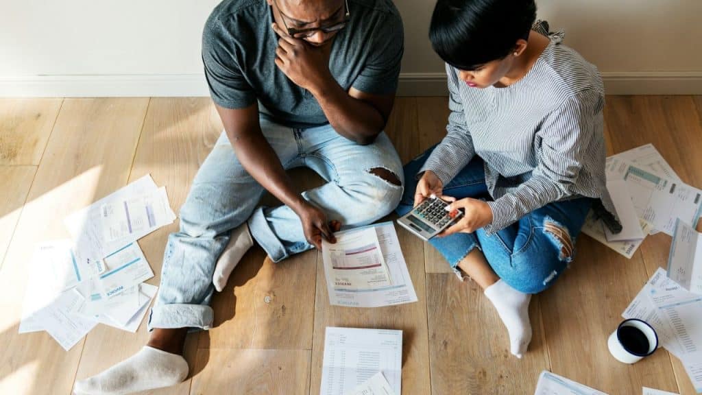 A high-angle view of a couple sitting on the floor, looking at bills and a calculator.