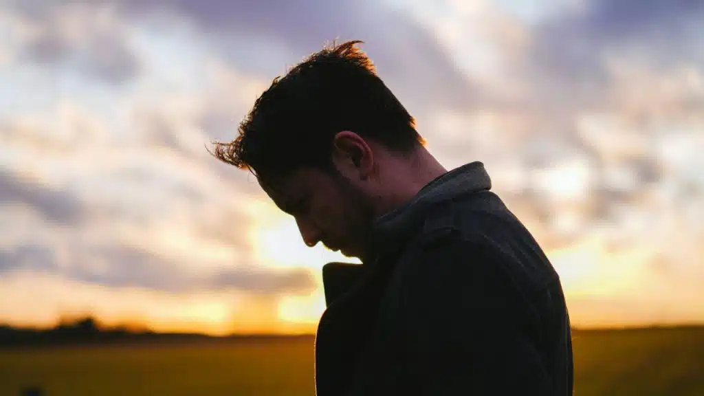 A silhouette of a man looking down at sunset, with a field in the background.