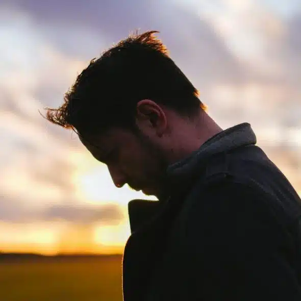 A silhouette of a man looking down at sunset, with a field in the background.