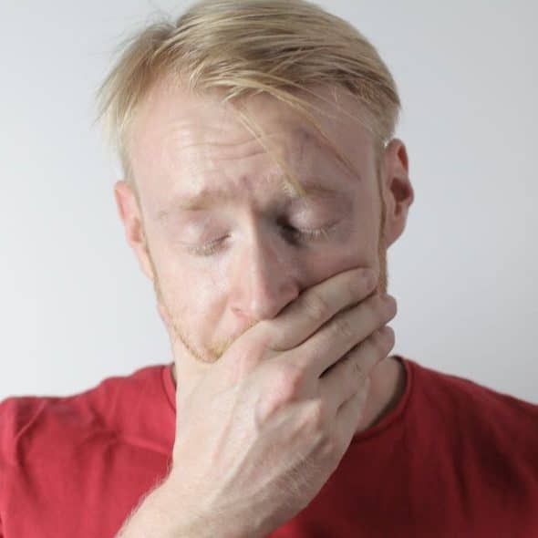 A man with blonde hair and a beard covers his mouth with his hand, looking pained.