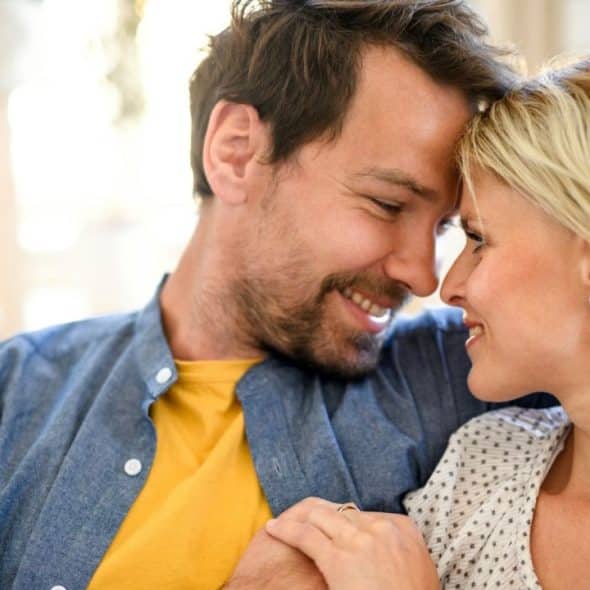 A man and a woman, smiling and with their foreheads touching, are looking at each other.