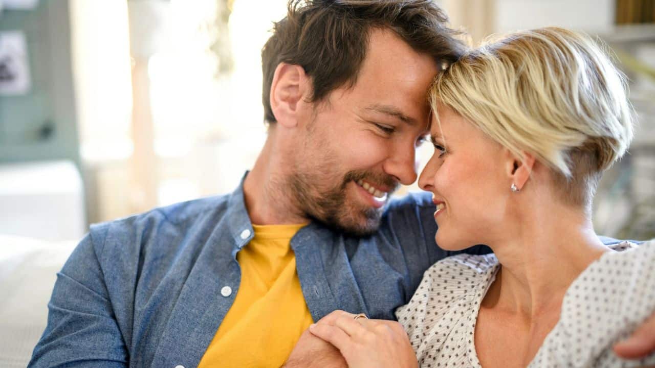 A man and a woman, smiling and with their foreheads touching, are looking at each other.