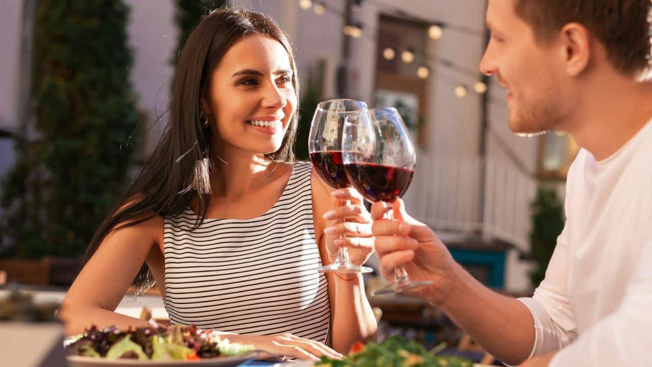 A man and a woman are clinking their wine glasses at an outdoor restaurant.