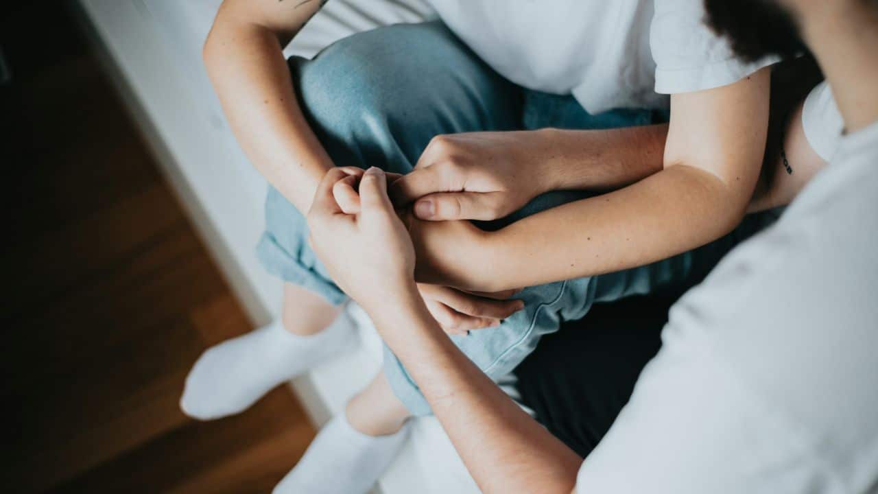 A top-down view shows two people holding hands, with one person wearing light blue jeans and white socks.
