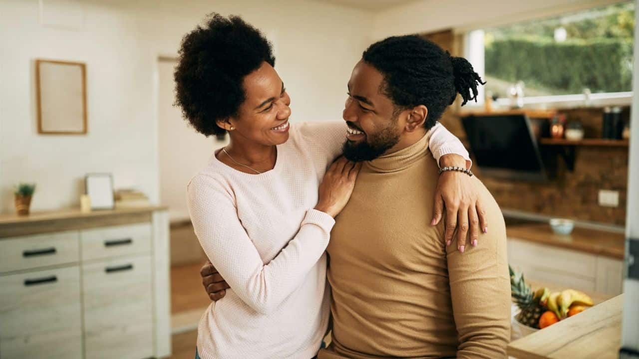 A smiling couple embraces and looks at each other in a kitchen.
