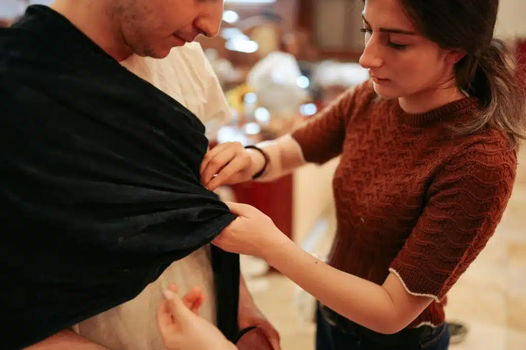 A woman helping a man to fix clothes.