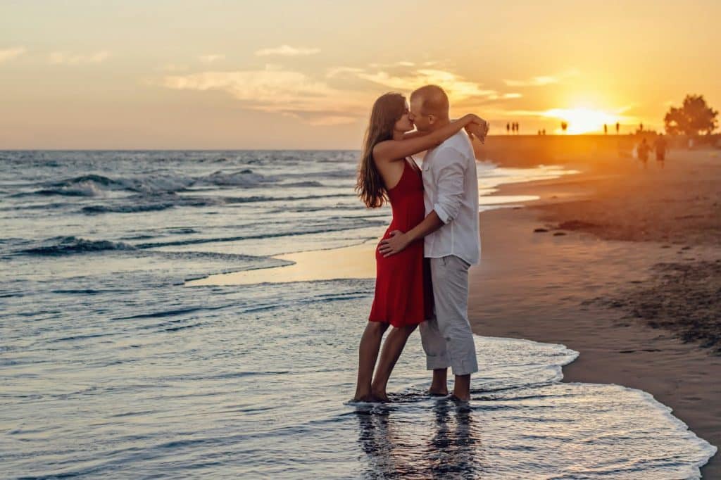 A man and woman kissing at the beach.