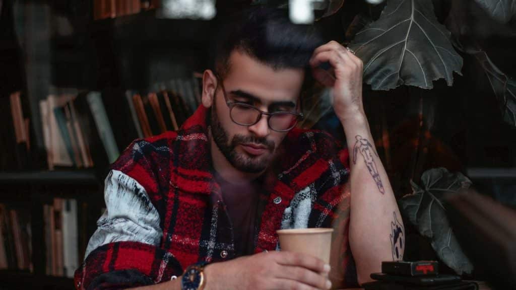 A man with headphones around his neck sits on a couch, looking at his smartphone.
