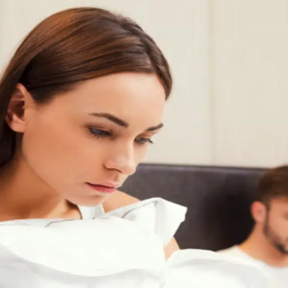 A woman. looking sad with her husband behind her