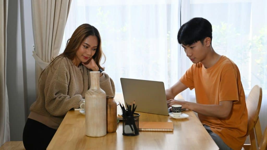 A young man and woman sit at a table, looking at a laptop.