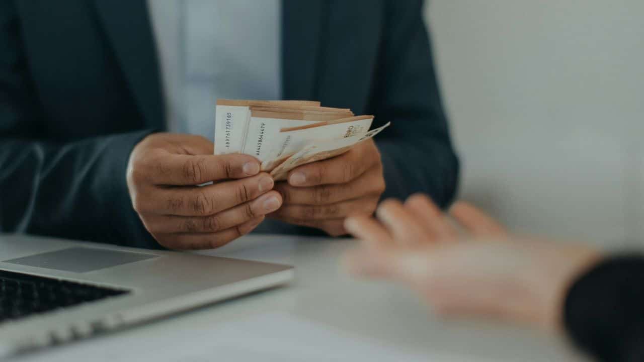 A person in a suit counts money, about to hand it to another person.