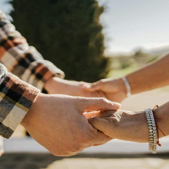 A close-up of two people holding hands outdoors.