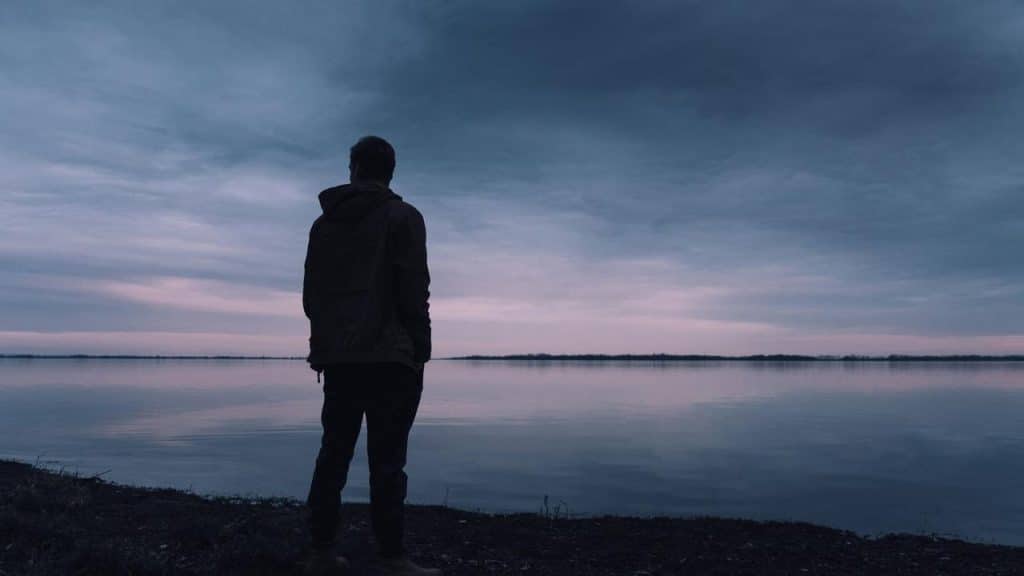 A silhouette of a man staring at the water at dusk.