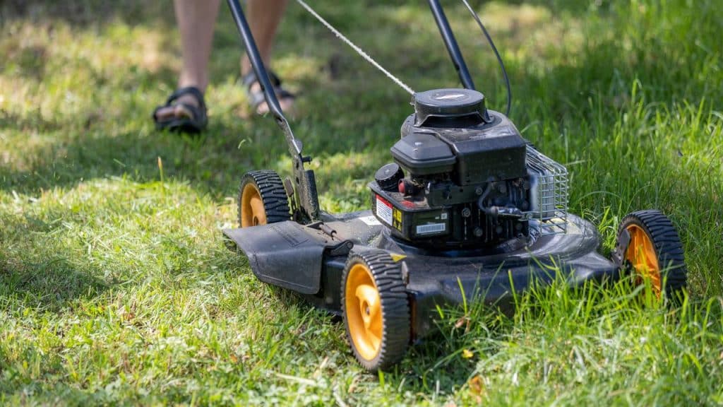 A black lawn mower with yellow wheels cutting grass.