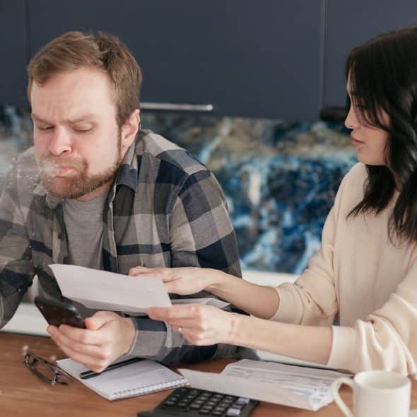 A man spits out a drink while looking at a phone, and a woman next to him holds papers.