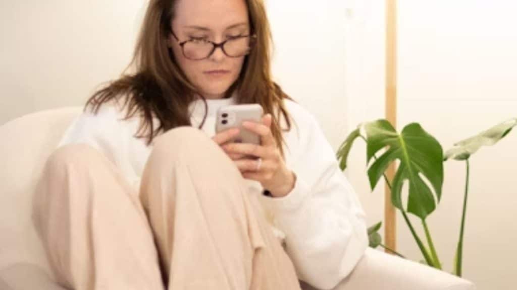 Woman scrolling on phone looking disheartened.