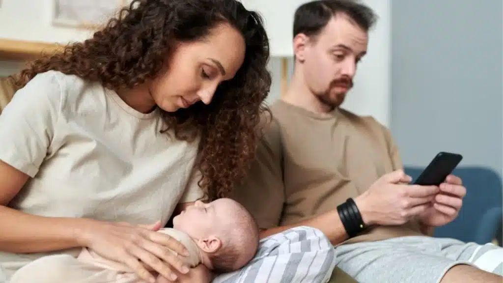 Mother multitasking with kids while dad sits nearby.