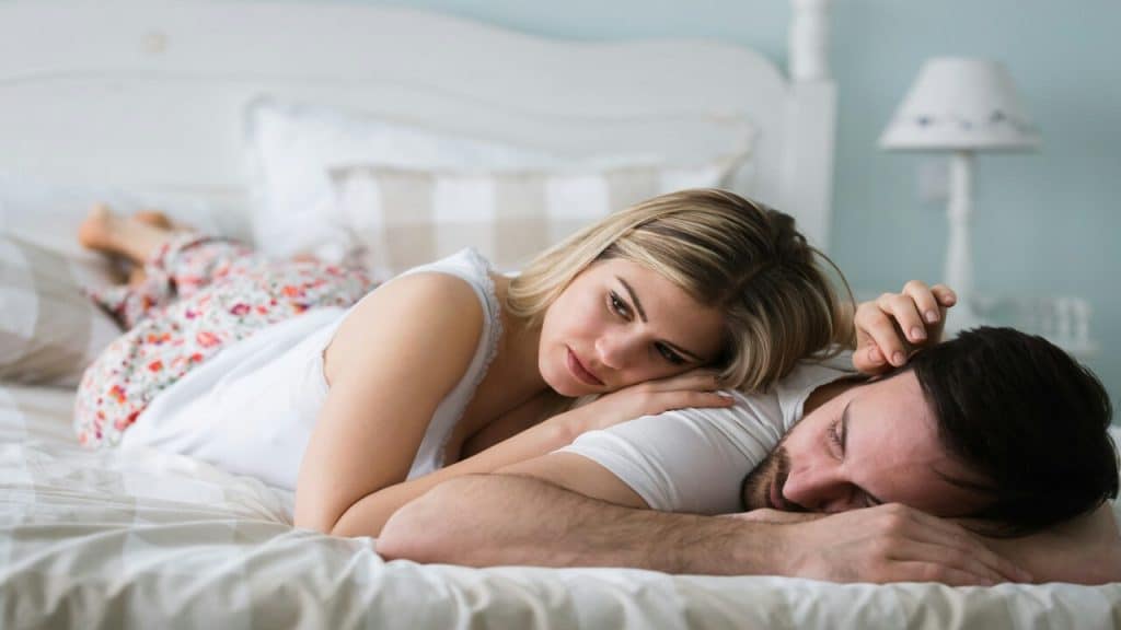 A woman looking sad while her husband sleeps.